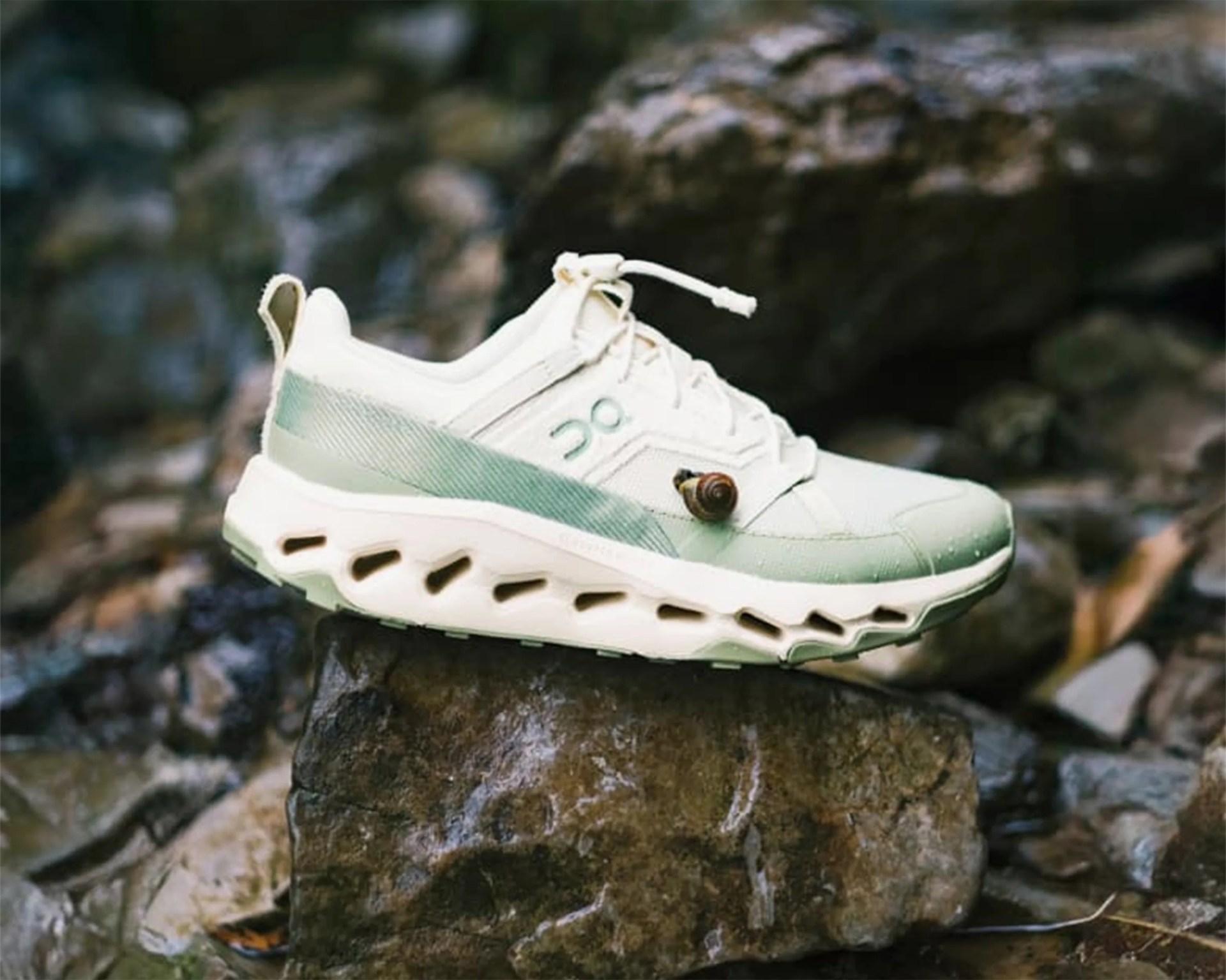 Light green and white athletic shoe with a unique sole design resting on a rock outdoors.