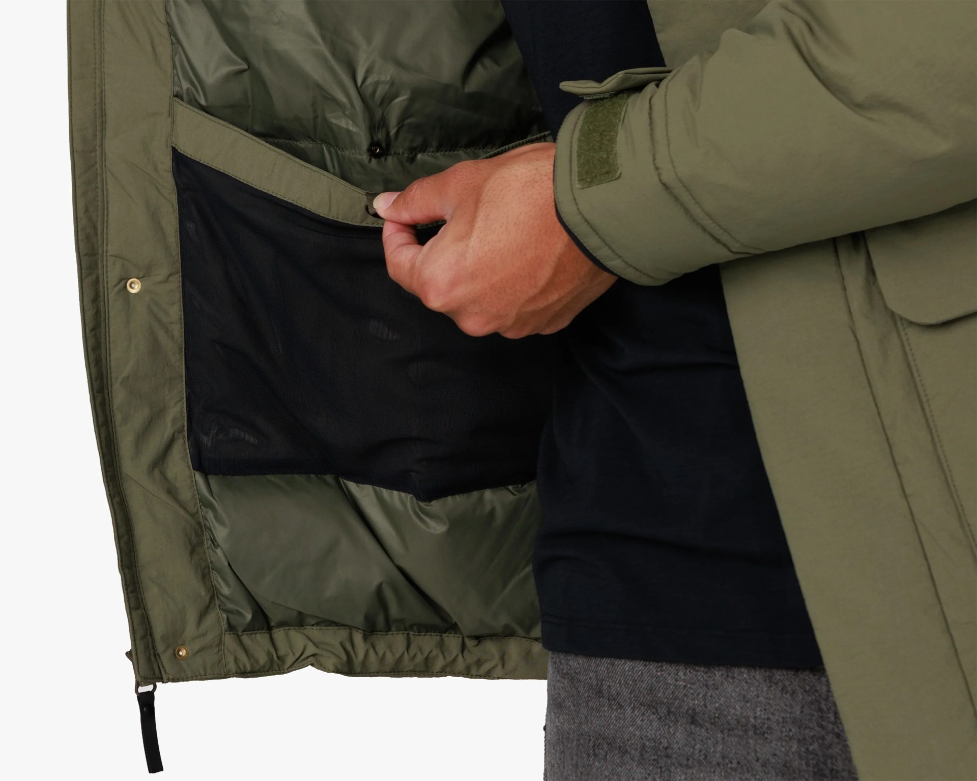 Hand holding open the inner pocket of an olive green jacket showing black mesh lining.