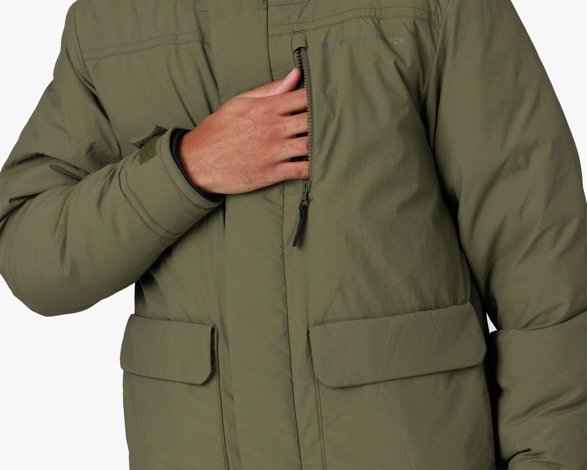 Olive-green padded jacket with zippered chest pocket and flap pockets, worn by a person with hand in chest pocket.