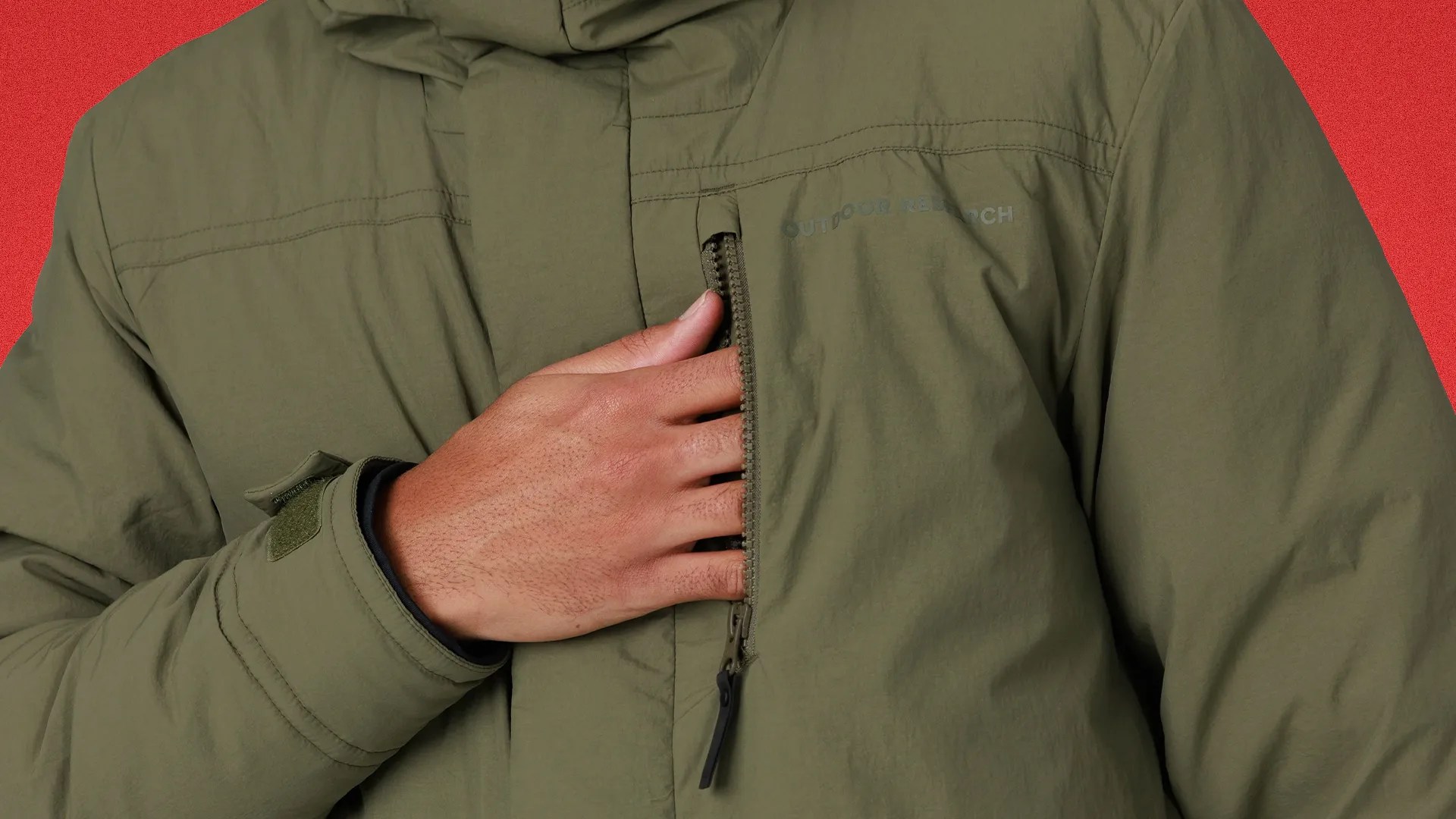 Hand reaching into the chest zipper pocket of an olive green Outdoor Research jacket.
