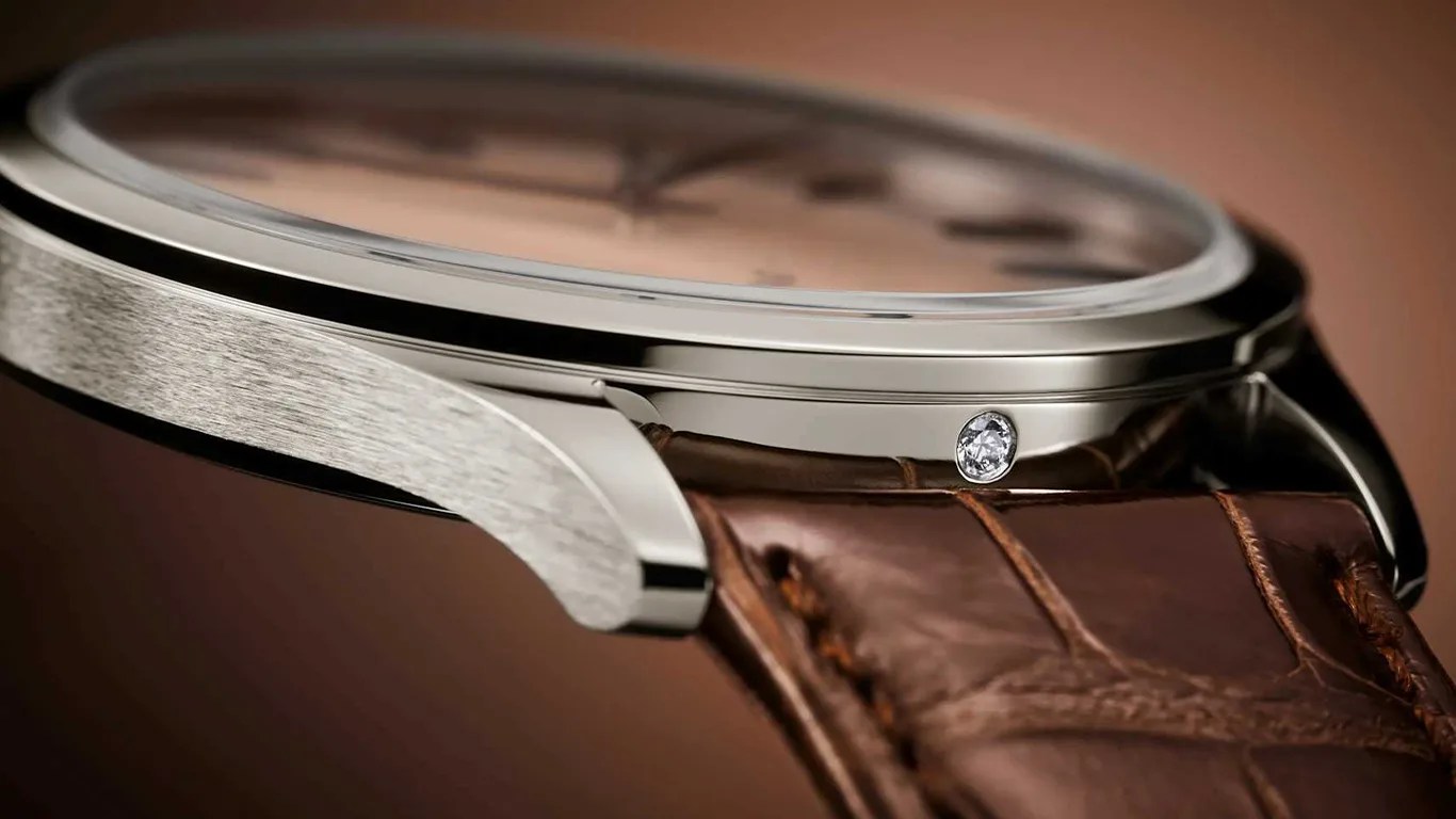 Close-up of a silver watch case with a diamond accent and a brown leather strap.