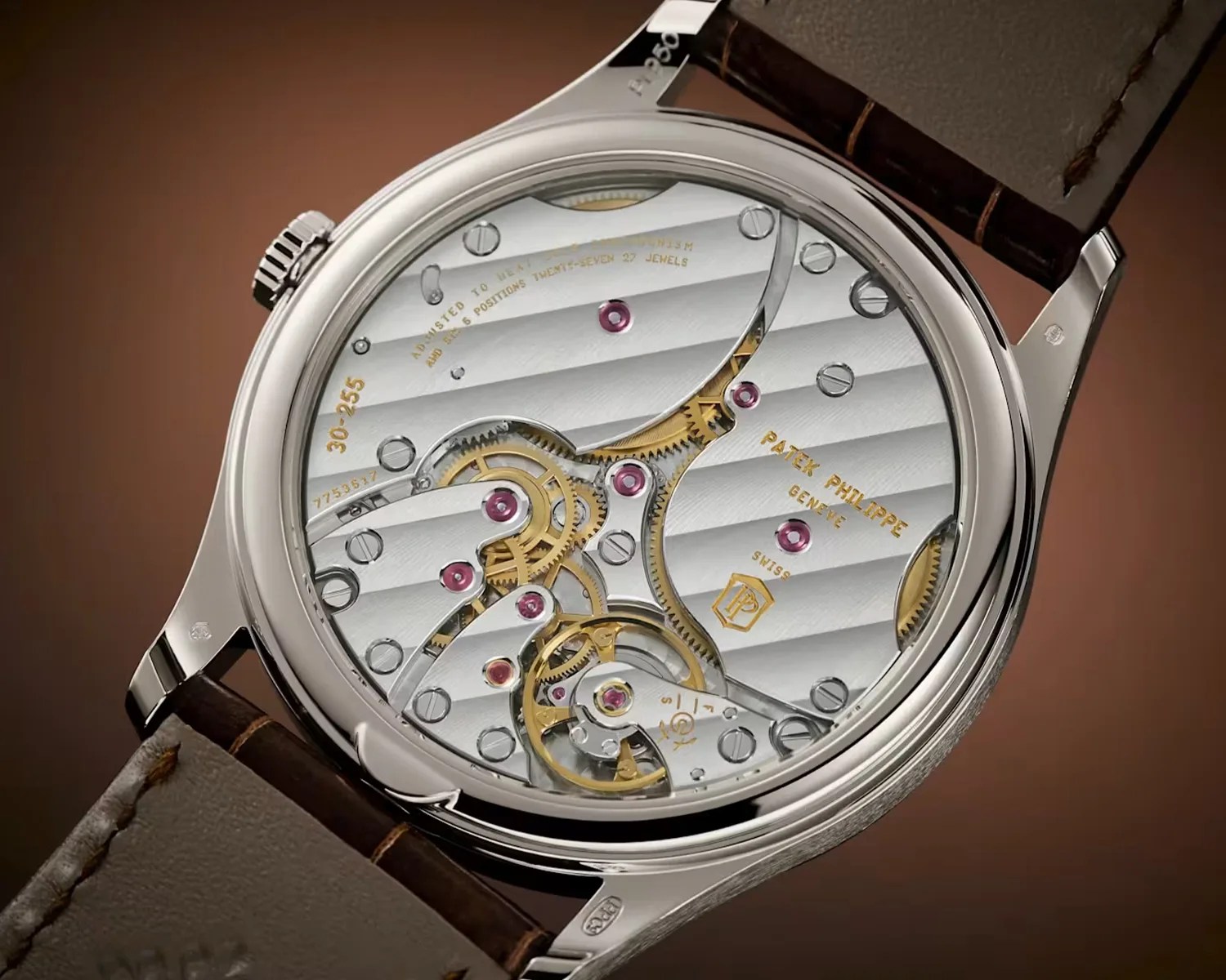 Close-up of a Patek Philippe watch movement with visible gears, jewels, and engraved text inside a polished metal case.