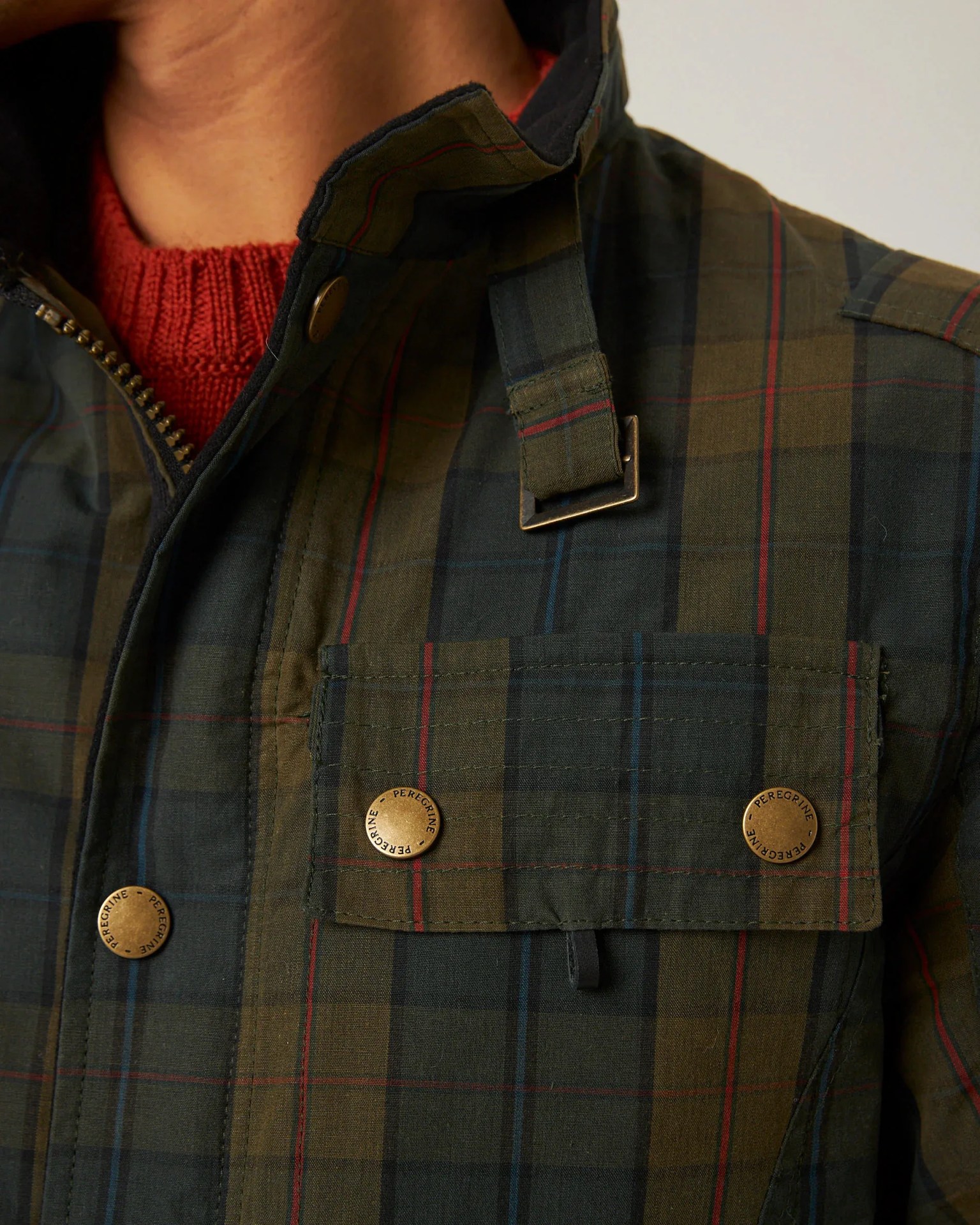 Close-up of a green and navy plaid jacket with red and blue stripes, brass snap buttons, and a buckle detail near the collar.