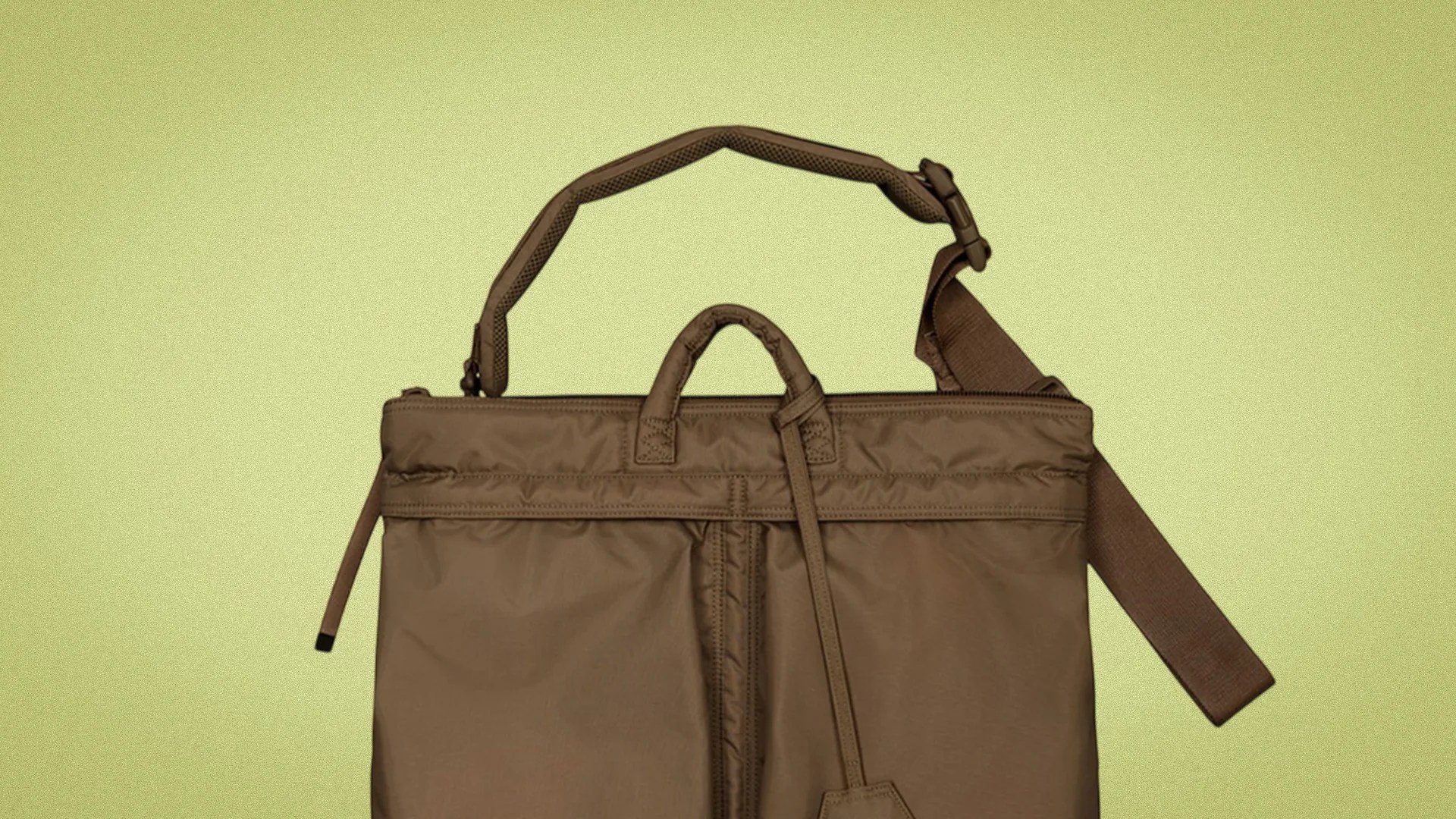Brown nylon tote bag with padded handles and adjustable shoulder strap against a light green background.