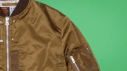 Brown bomber jacket with silver zipper and snap buttons on a green background.