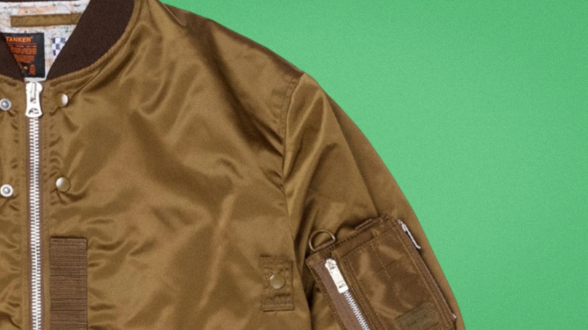 Brown bomber jacket with silver zipper and snap buttons on a green background.