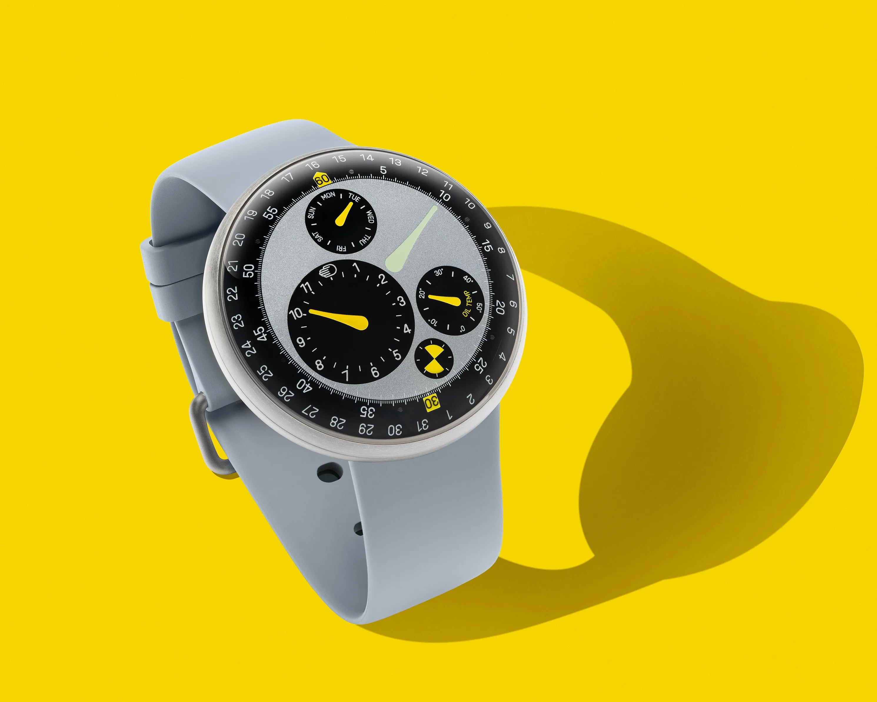 Round silver watch with a light blue silicone strap and a multi-dial gray and black face on a yellow background.