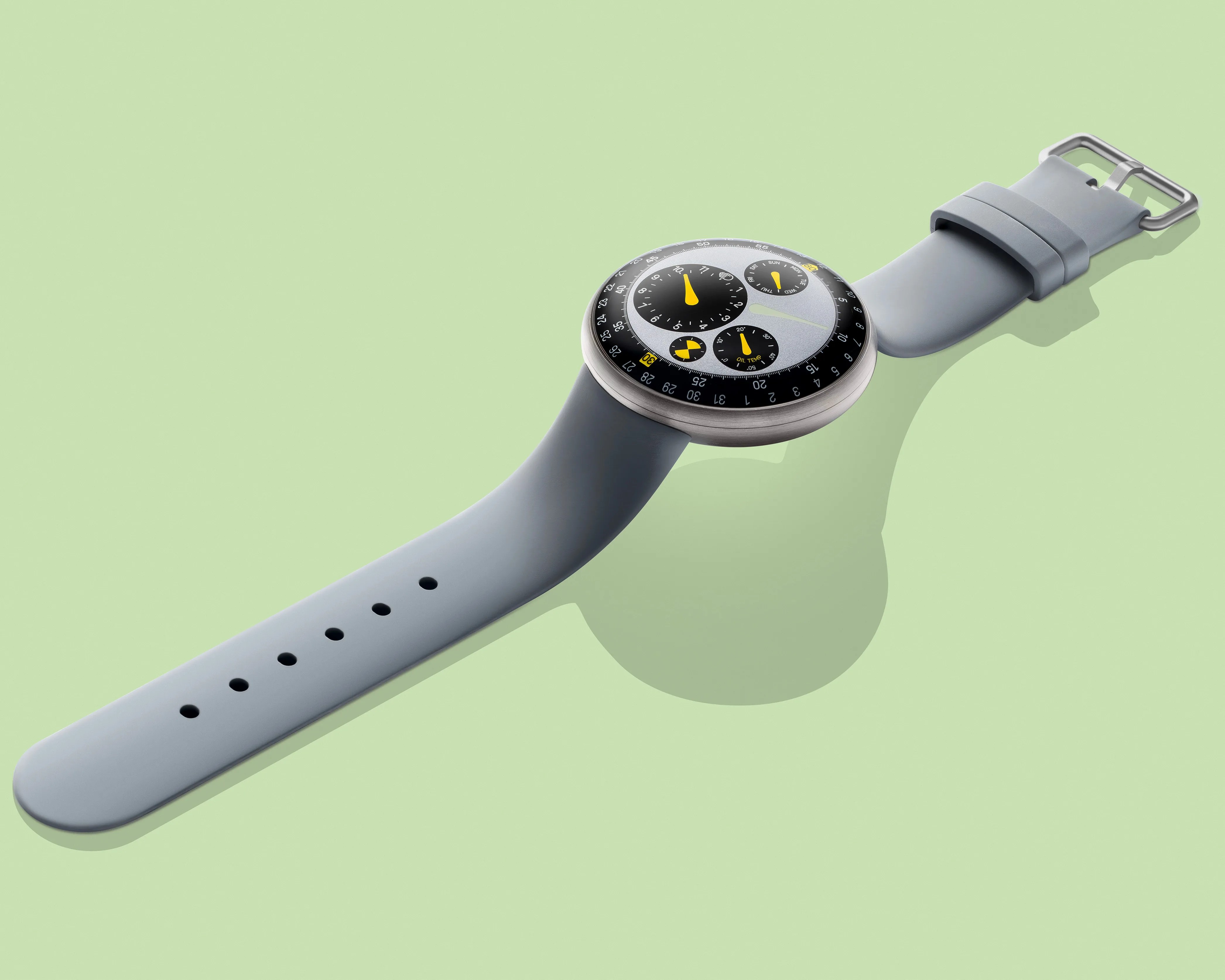Round silver watch with black and yellow dial and light gray silicone strap on a pale green background.