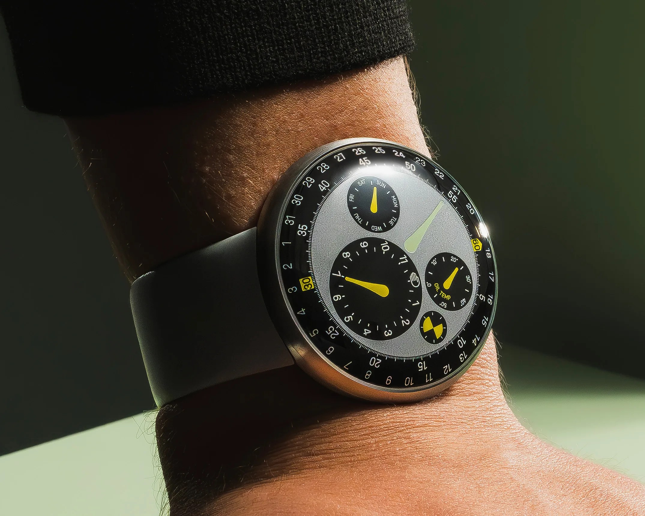 Round silver watch with black and yellow dials and a gray strap worn on a wrist.