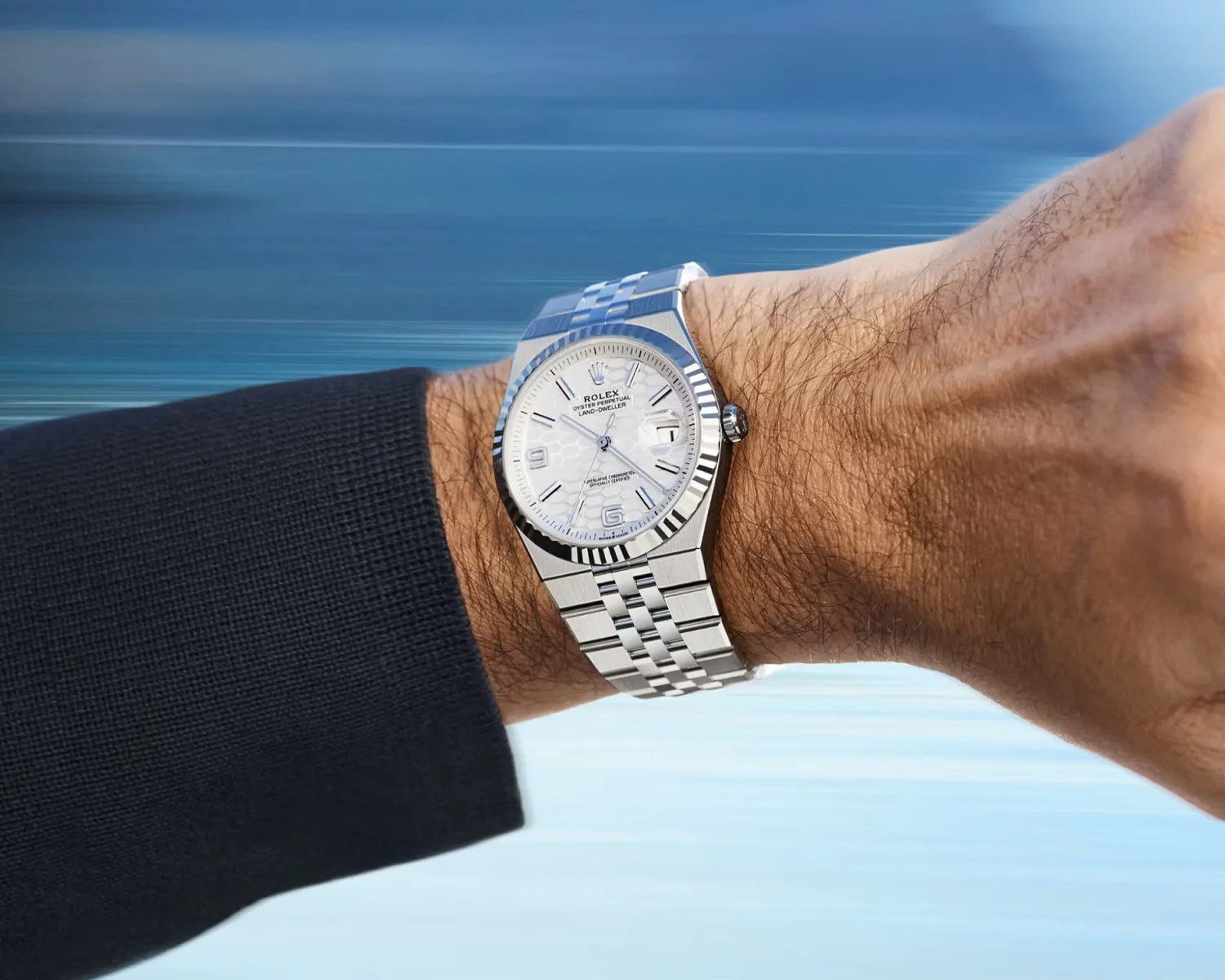 Silver Rolex Oyster Perpetual Land-Dweller watch with white textured dial on a wrist.