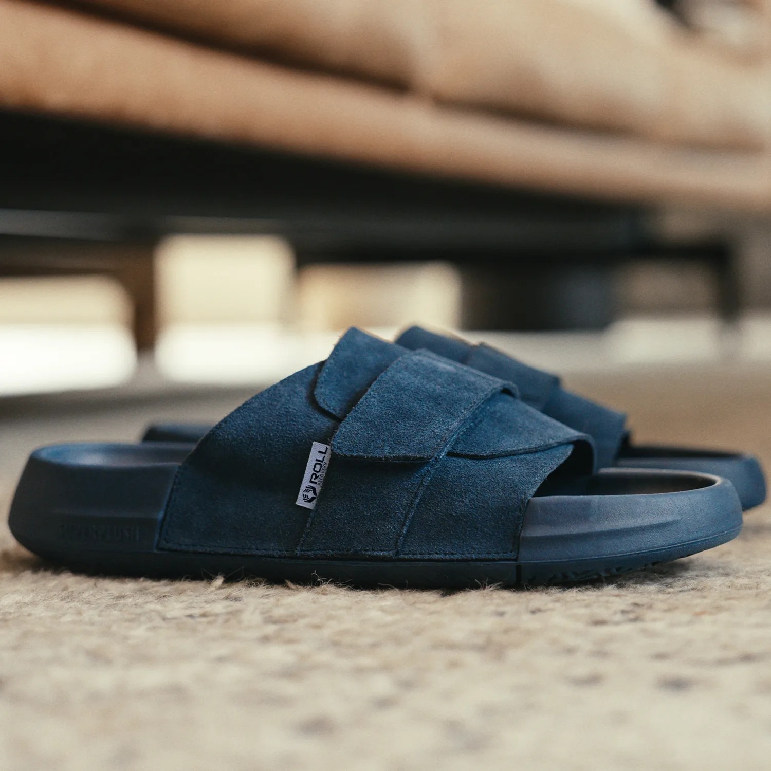 Pair of navy blue suede slide sandals with adjustable straps on a beige carpet.
