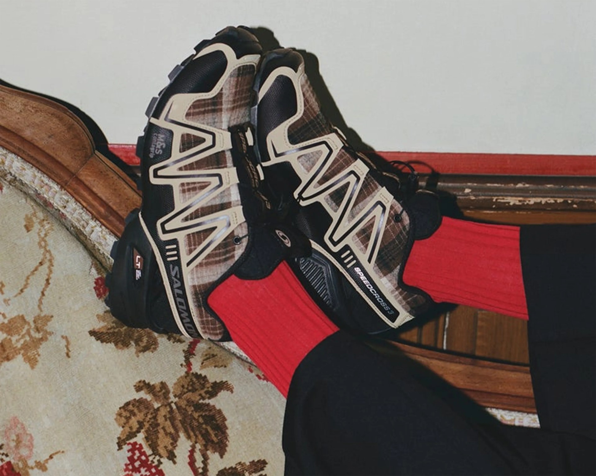 Pair of brown and black Salomon Speedcross 3 trail running shoes worn with bright red ribbed socks.