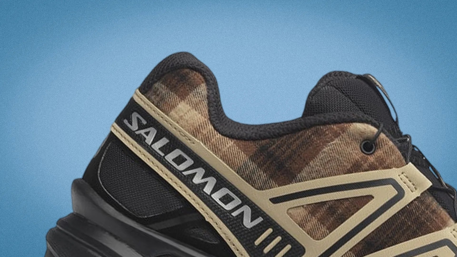 Close-up of a brown and black Salomon sneaker with beige accents against a blue background.