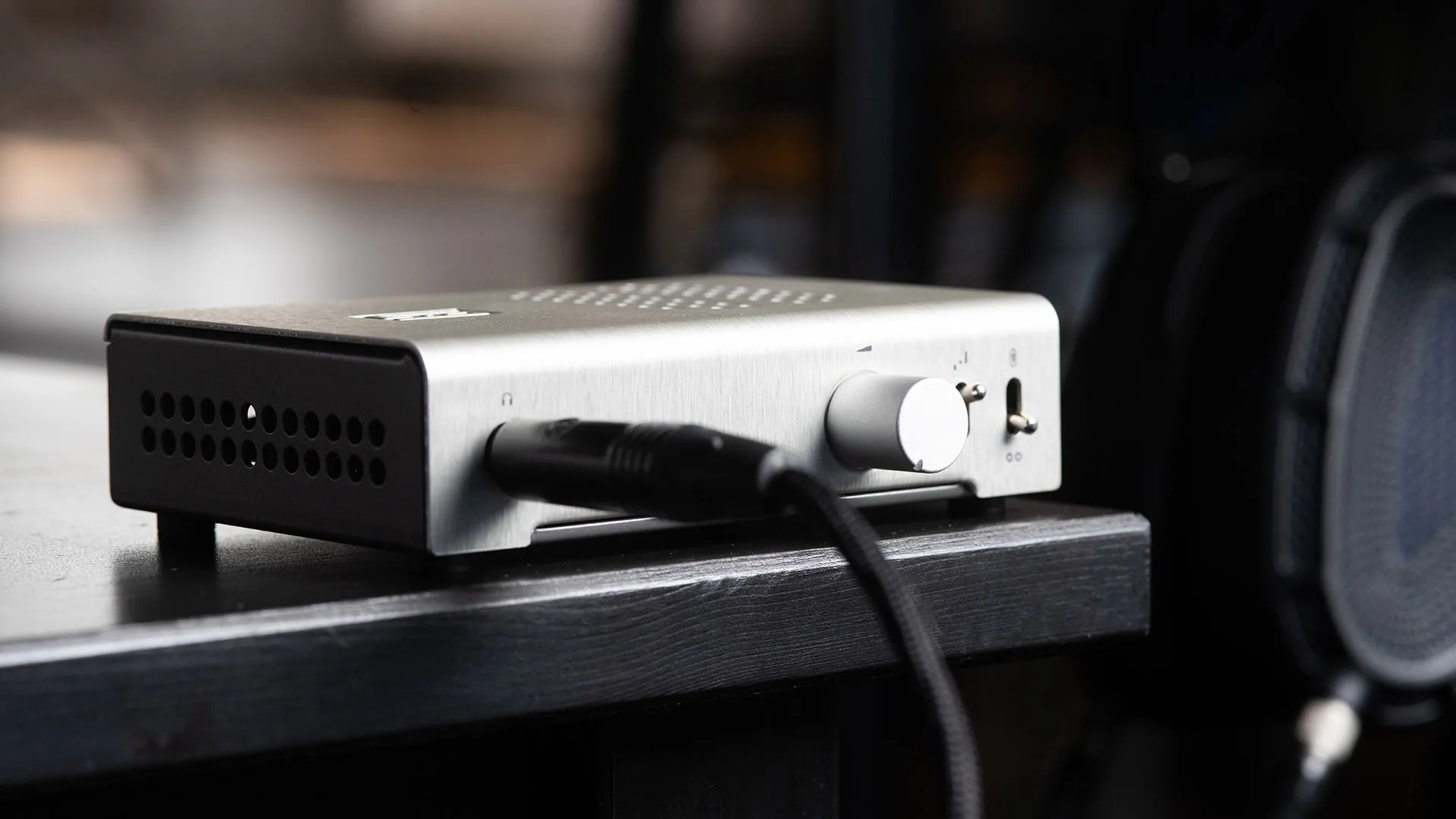 Silver audio amplifier with a volume knob and connected cable on a black wooden surface.