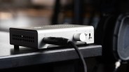 Silver audio amplifier with a volume knob and connected cable on a black wooden surface.