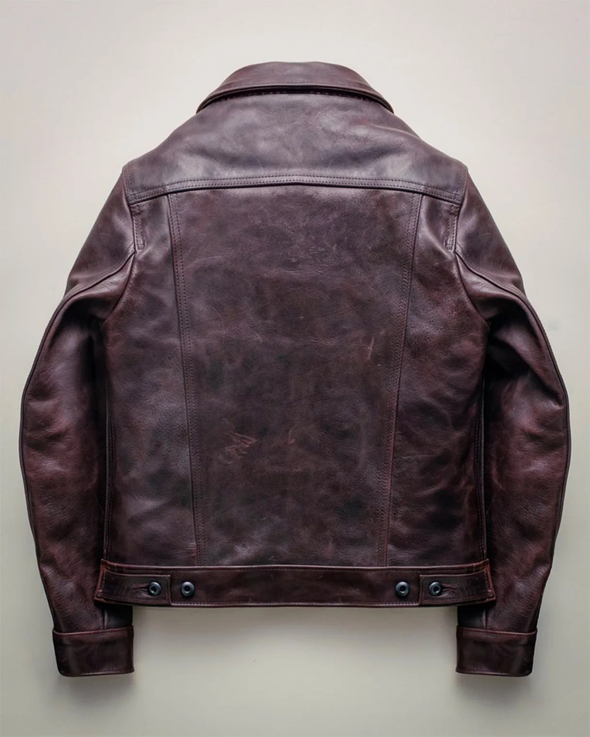 Dark brown leather jacket with buttoned adjustable waist straps laid flat showing the back.