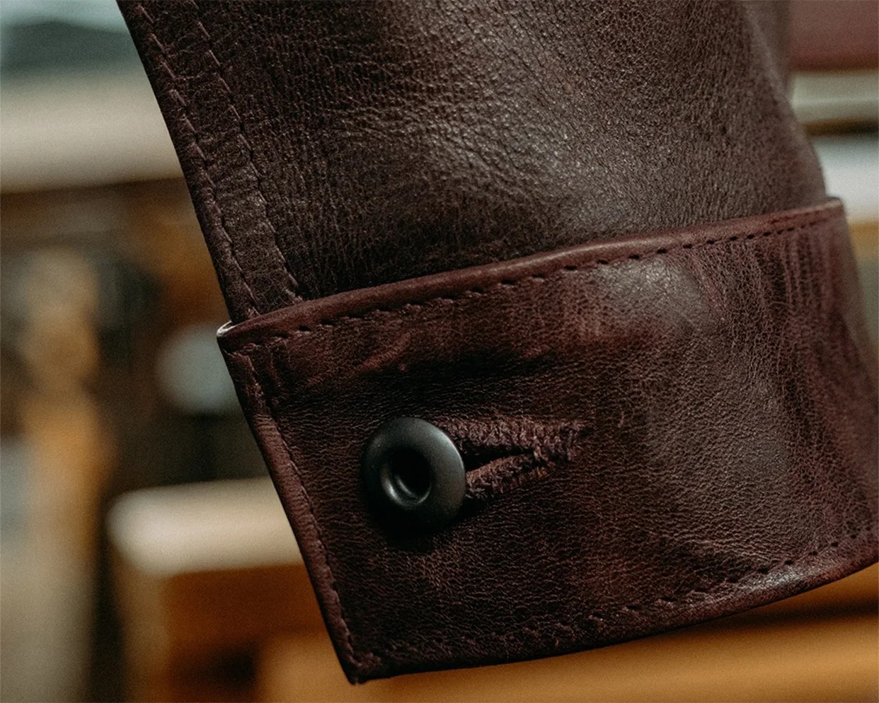 Close-up of a dark brown leather sleeve cuff with a black button and detailed stitching.