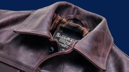 Close-up of a brown leather jacket collar with a plaid fabric lining and a visible brand label inside.