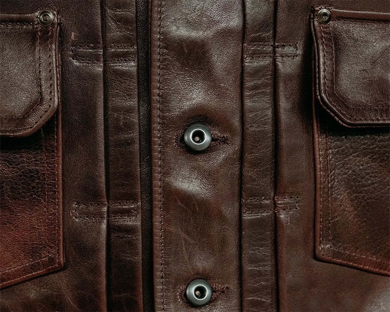 Close-up of dark brown leather jacket with snap buttons and two flap pockets.