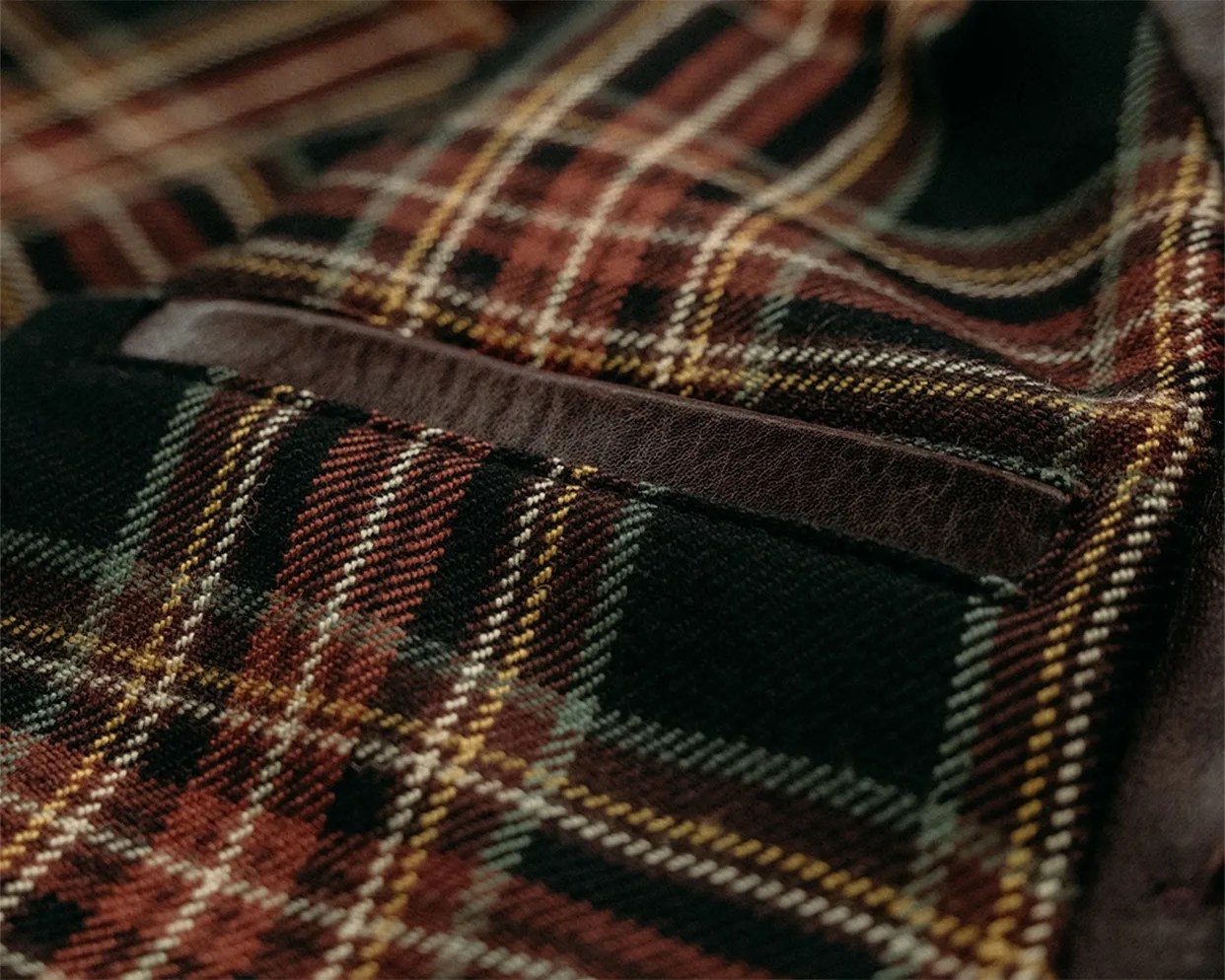 Close-up of a brown, black, and yellow plaid fabric with a dark brown leather-trimmed pocket.