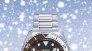 Close-up of a Seiko stainless steel wristwatch with a brown dial and rotating bezel against a snowy background.