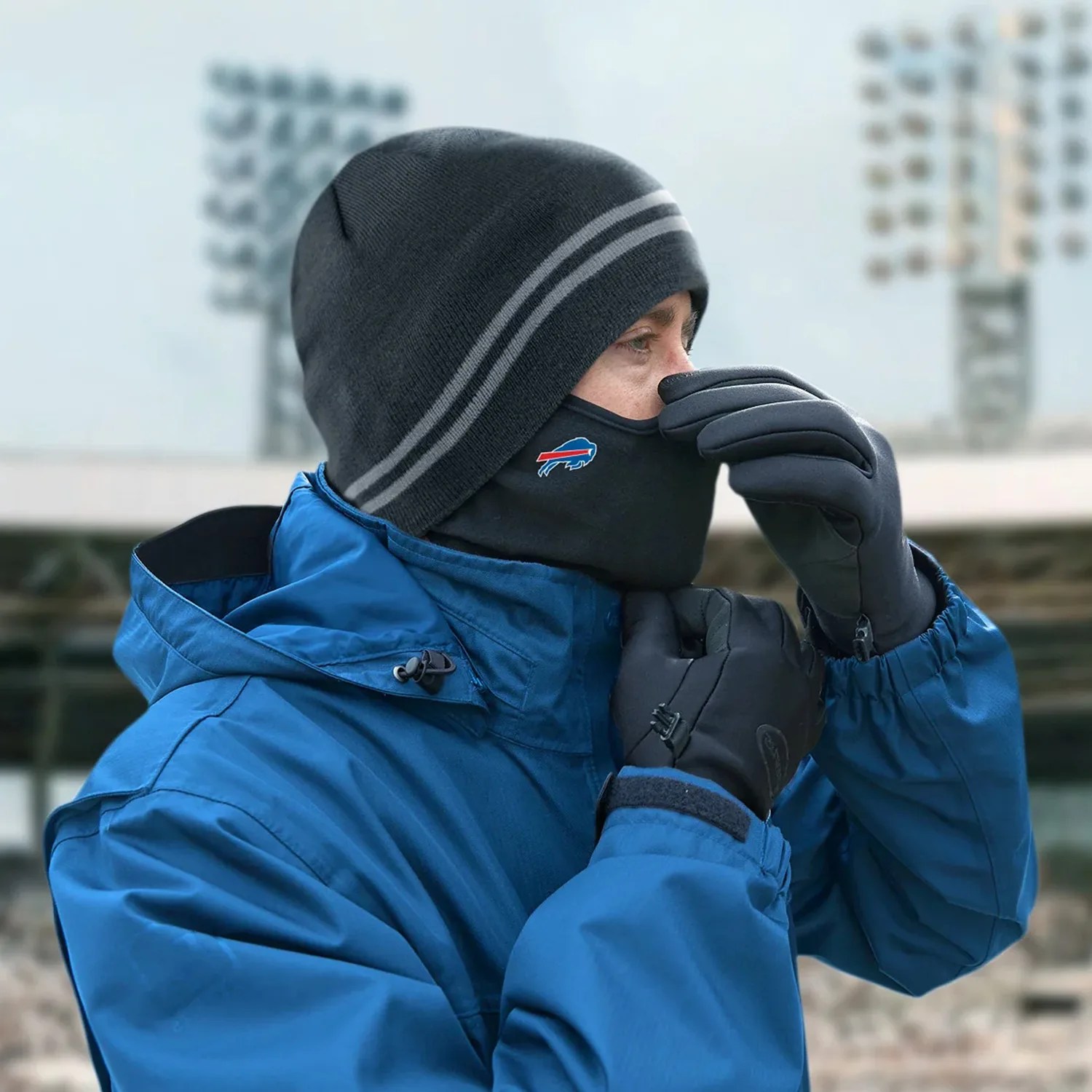 Person wearing a blue jacket, black gloves, black beanie with gray stripes, and a black face mask with a blue and red buffalo logo.