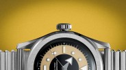 Close-up of a stainless steel wristwatch with a beige and black dial and a metal bracelet against a yellow background.