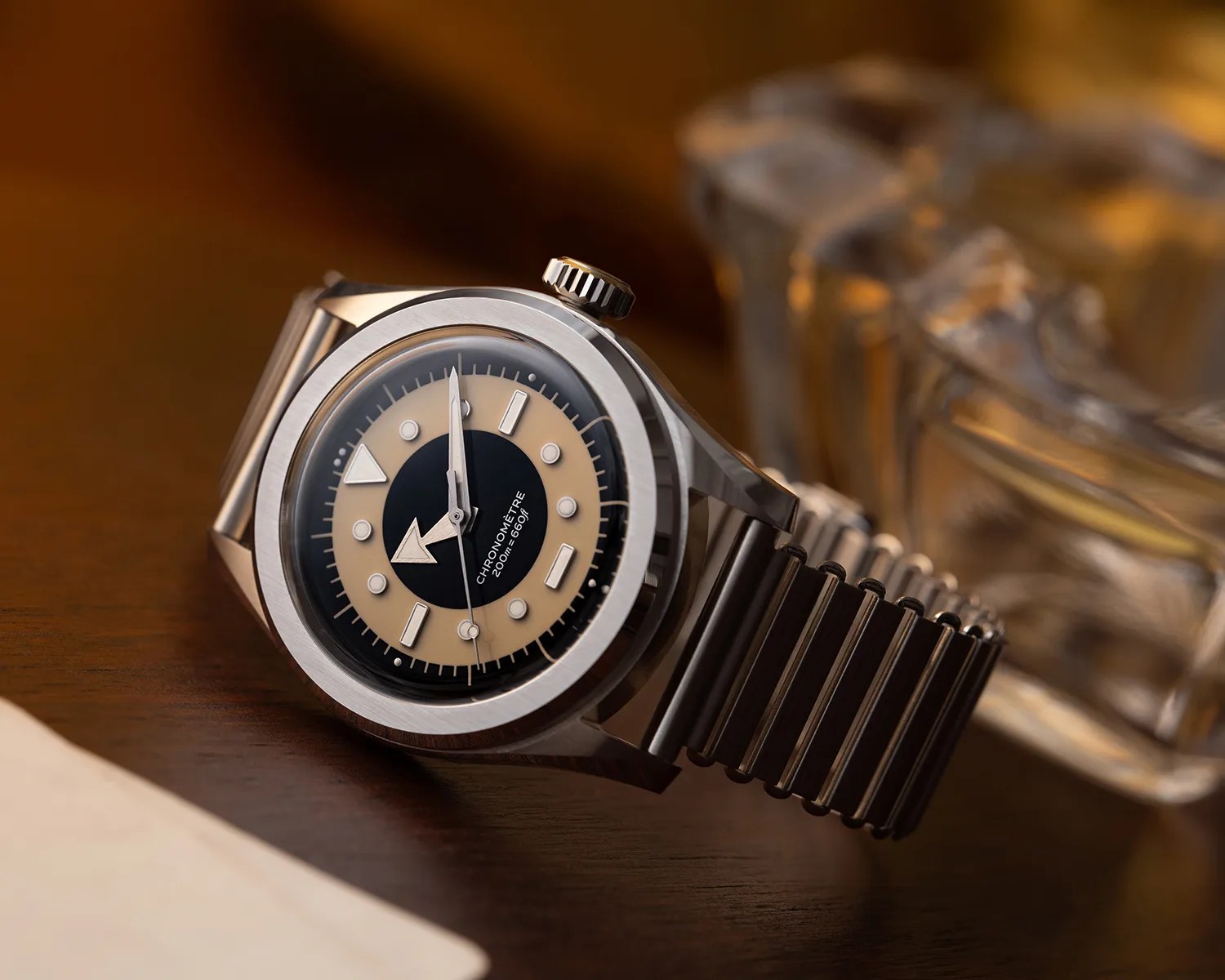 Stainless steel wristwatch with black and beige dial and metal bracelet on a wooden surface.