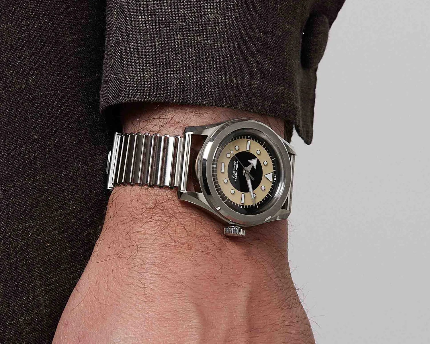 Silver metal wristwatch with a beige and black dial worn on a wrist with a dark brown sleeve.