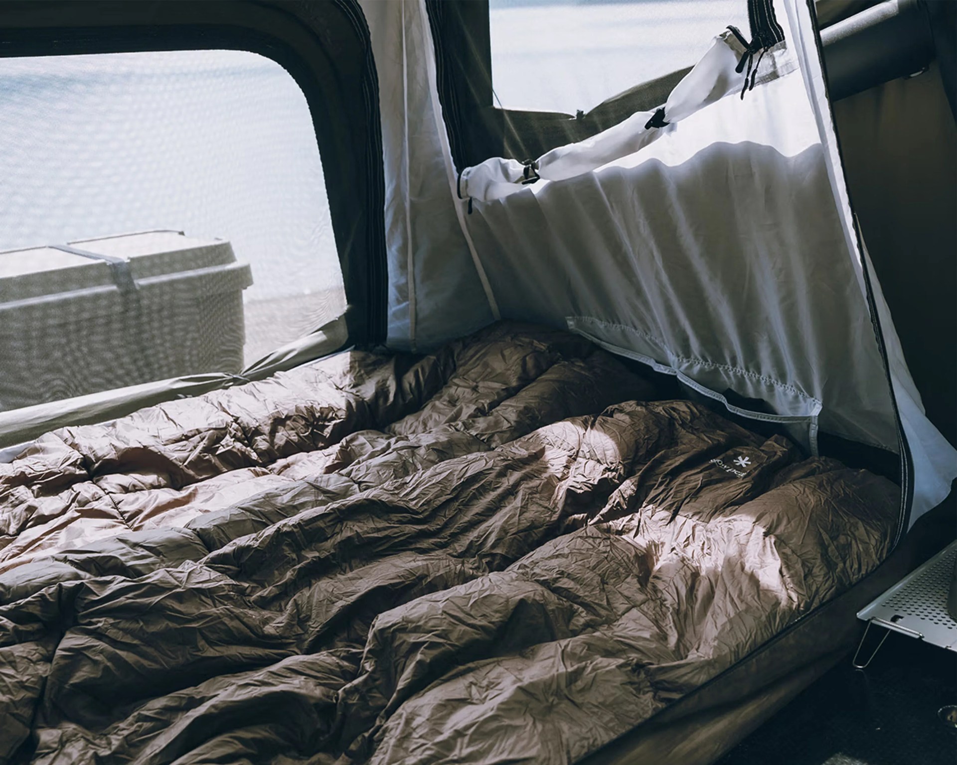 Brown sleeping bag laid out inside a tent with mesh windows and a cooler visible outside.