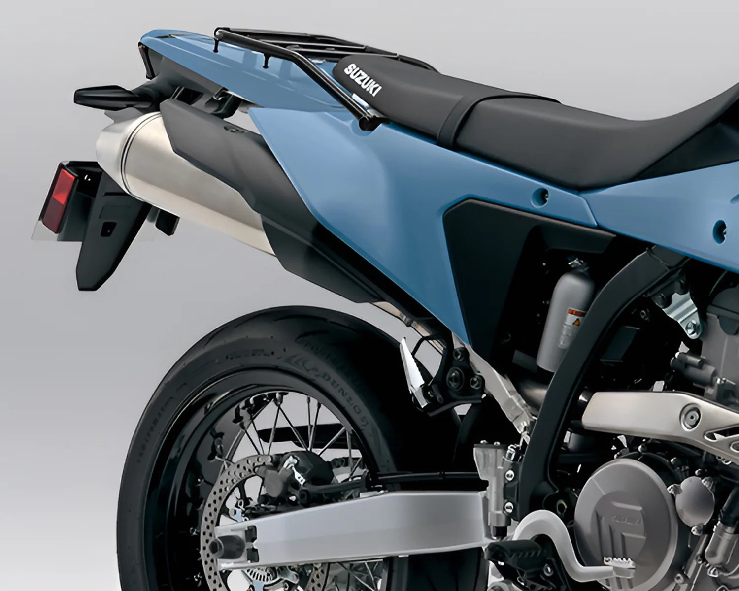 Rear section of a blue Suzuki motorcycle showing the exhaust, rear wheel, and part of the engine.