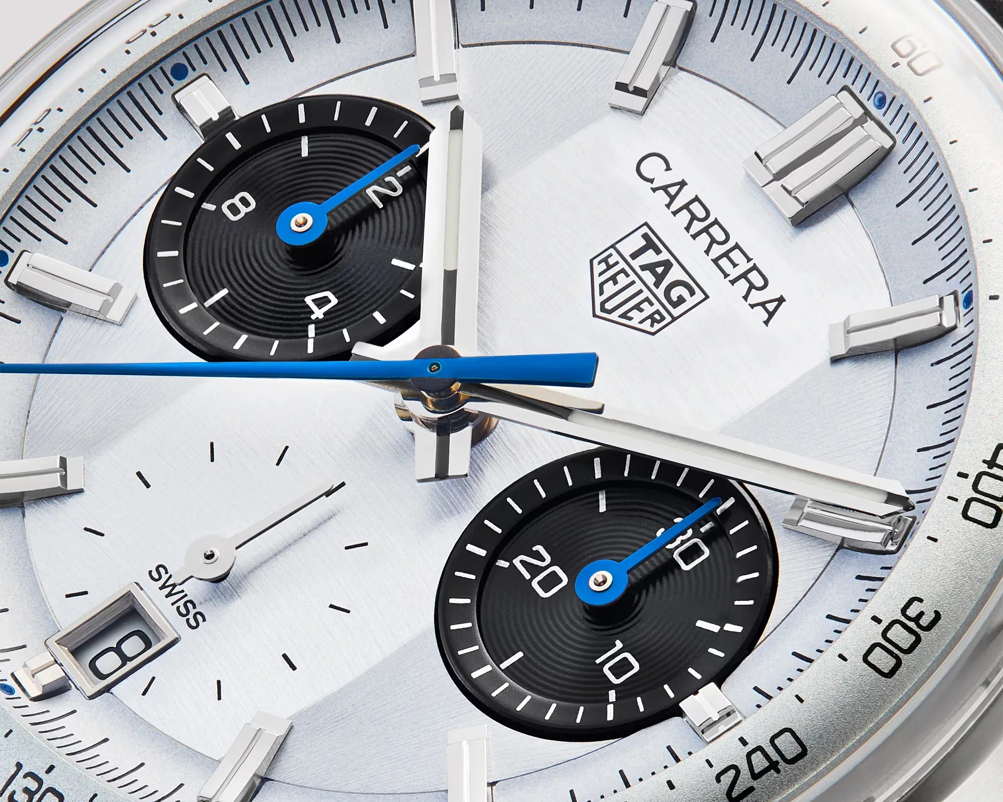 Close-up of a TAG Heuer Carrera watch face with silver dial, black subdials, blue and silver hands, and date window.