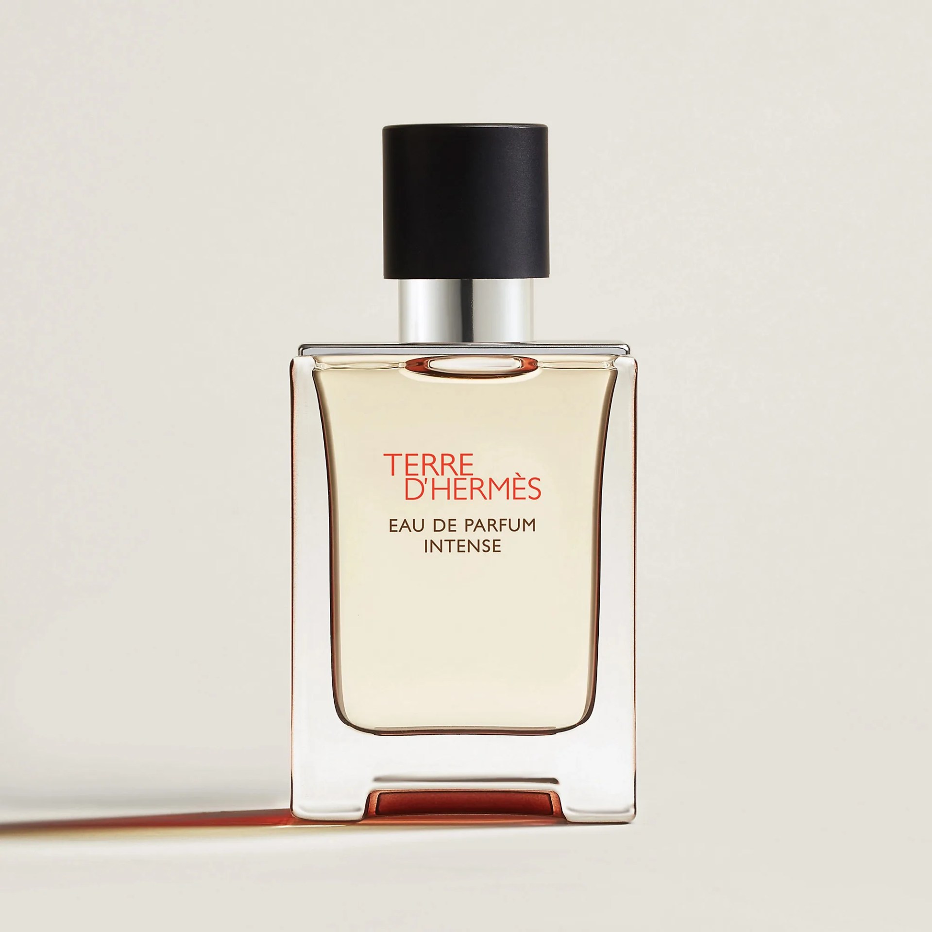 Clear rectangular glass perfume bottle with beige liquid, black cap, and "Terre d'Hermès Eau de Parfum Intense" text.