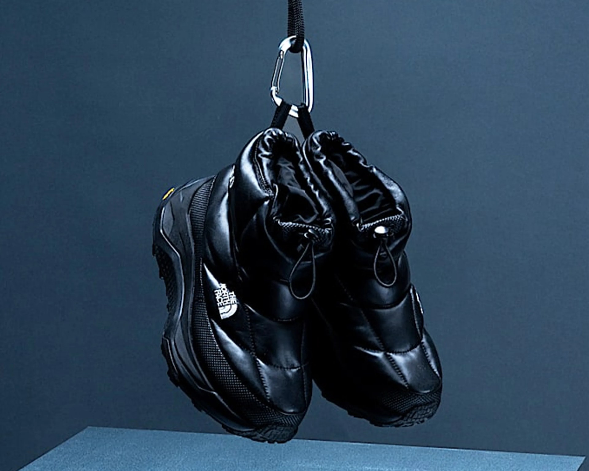 Pair of black insulated winter shoes with The North Face logo hanging from a carabiner clip.