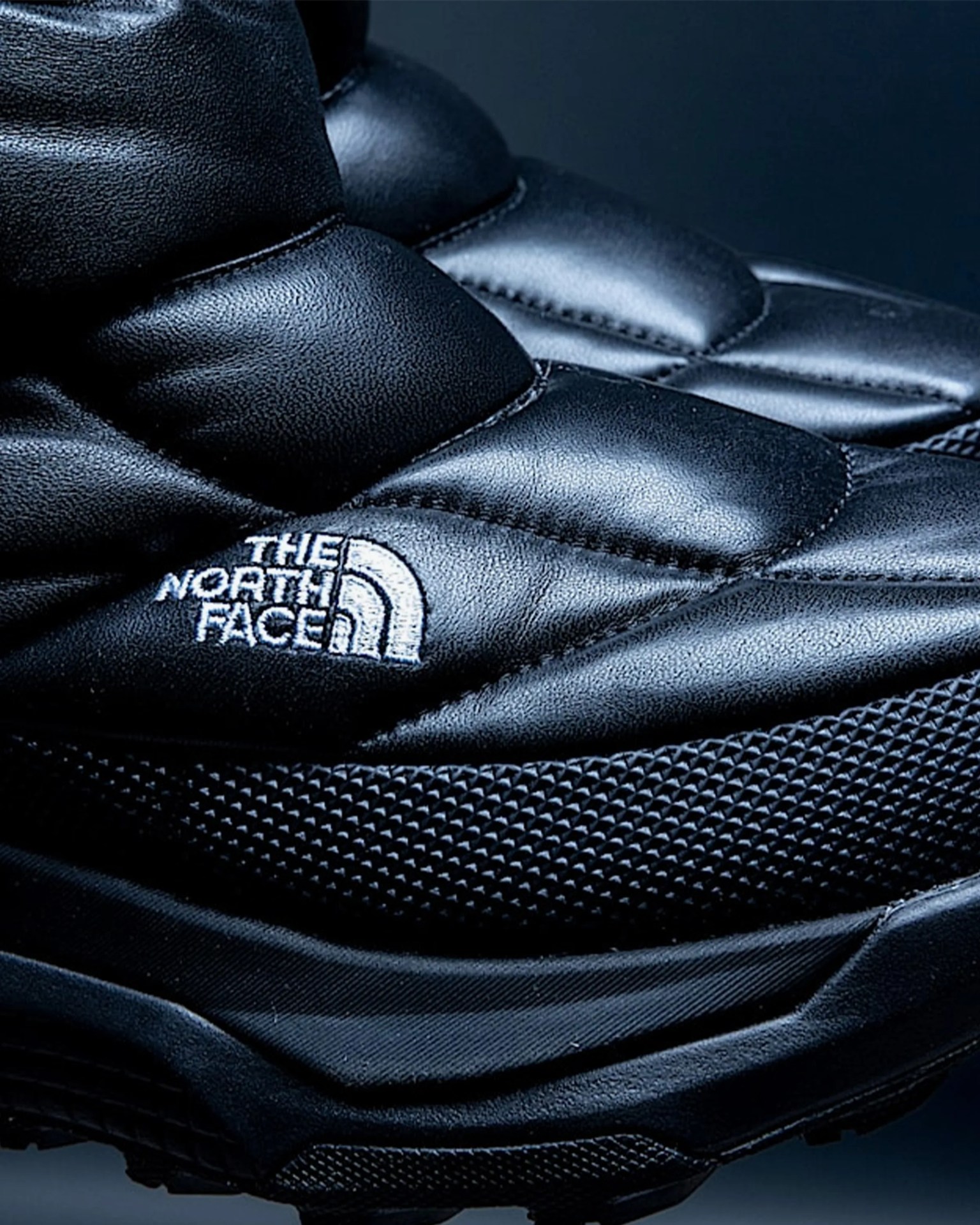 Close-up of black padded The North Face shoe with textured midsole and white embroidered logo.