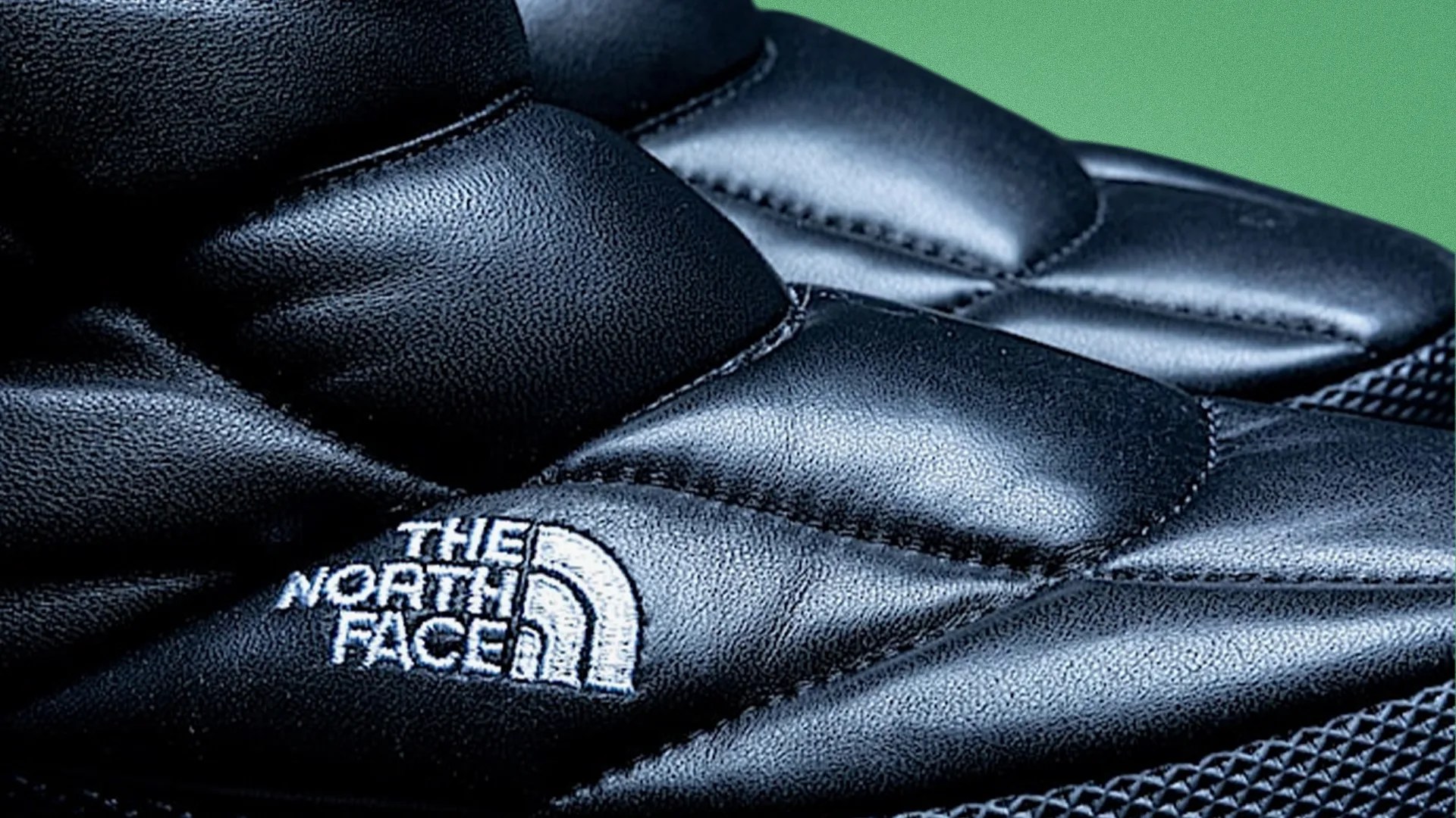 Close-up of black padded fabric with white embroidered The North Face logo.