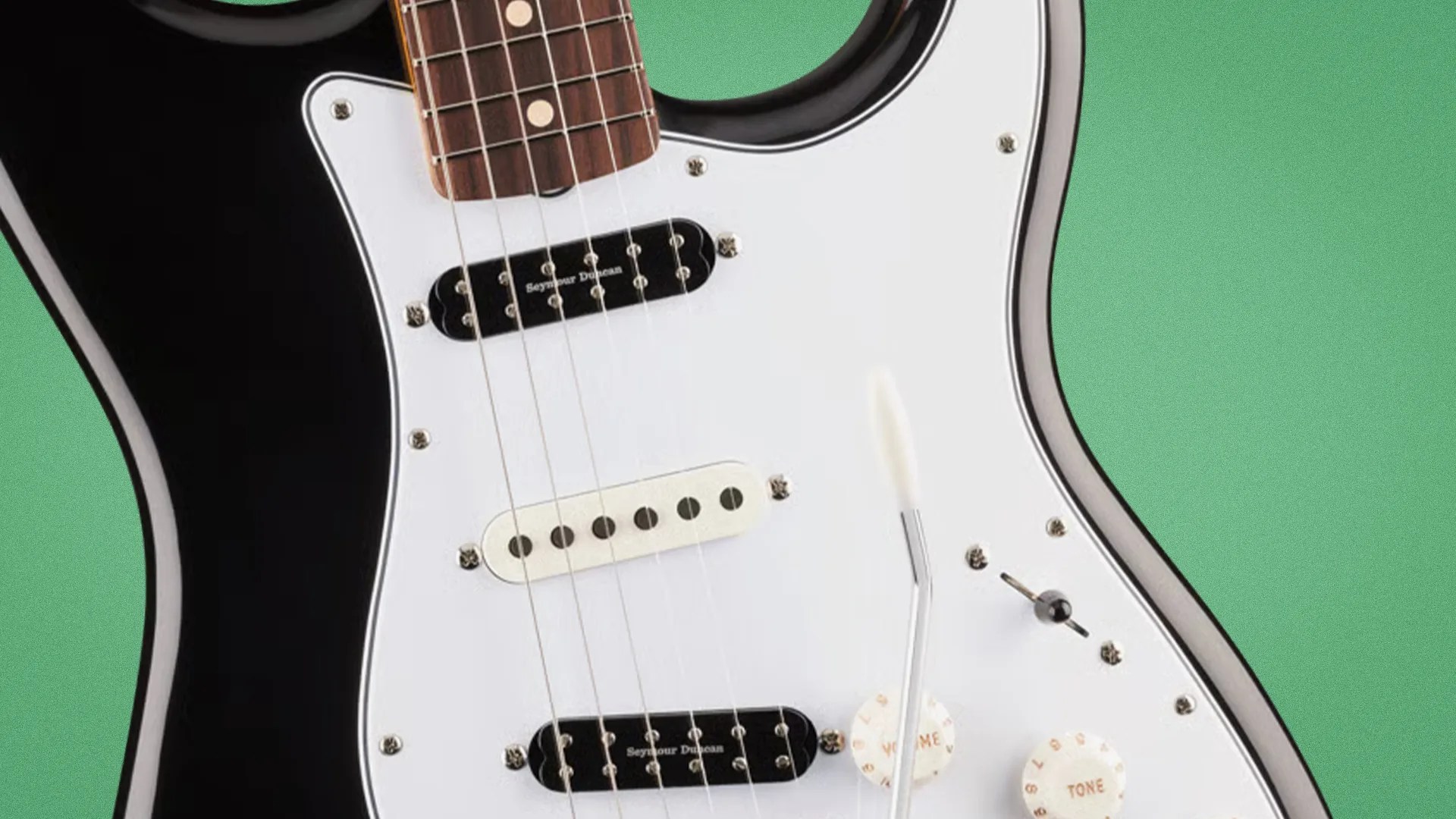 Close-up of a black electric guitar body with white pickguard, three pickups, two control knobs, and a tremolo arm.