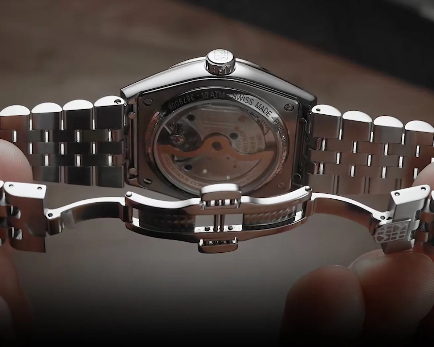 Close-up of a stainless steel watch with a transparent case back showing the automatic movement and a metal bracelet clasp.