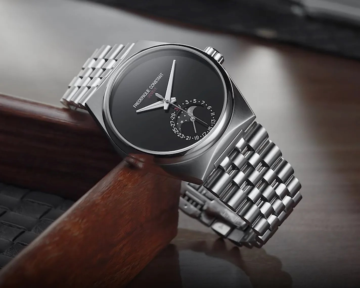 Silver metal bracelet watch with black dial and moon phase date display on wooden surface.