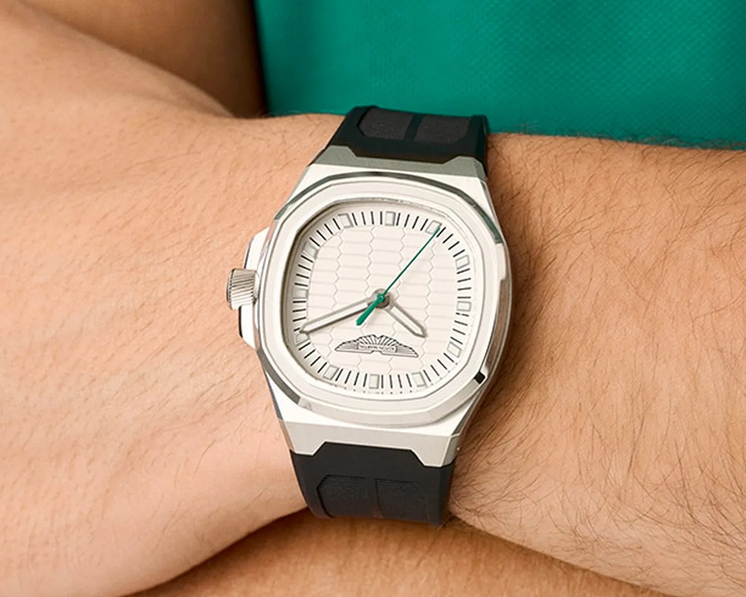 Silver square watch with white textured dial and black rubber strap worn on a wrist.
