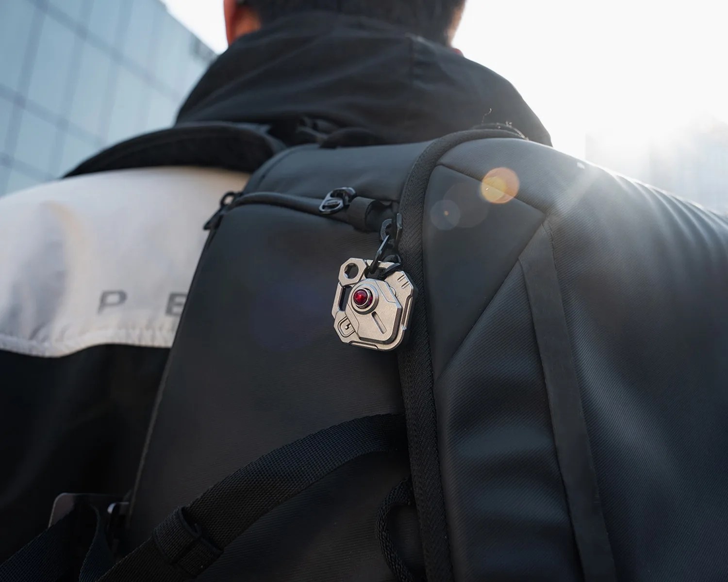 Silver mechanical keychain with a red gem attached to the zipper of a black backpack worn by a person.