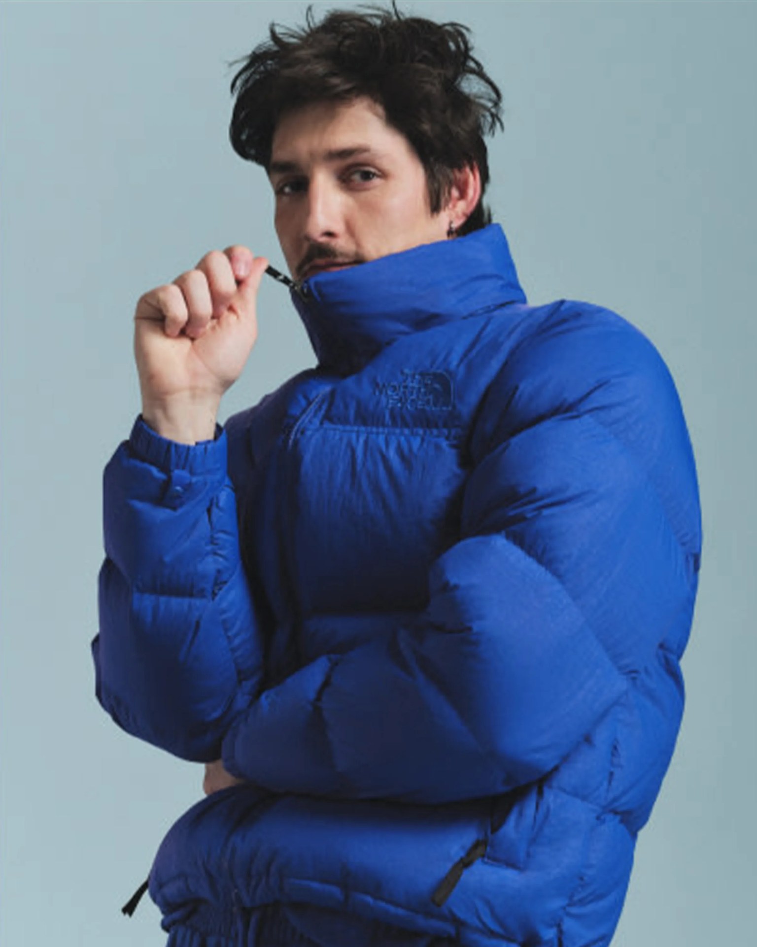Man wearing a bright blue North Face puffer jacket with a high collar zipped up.
