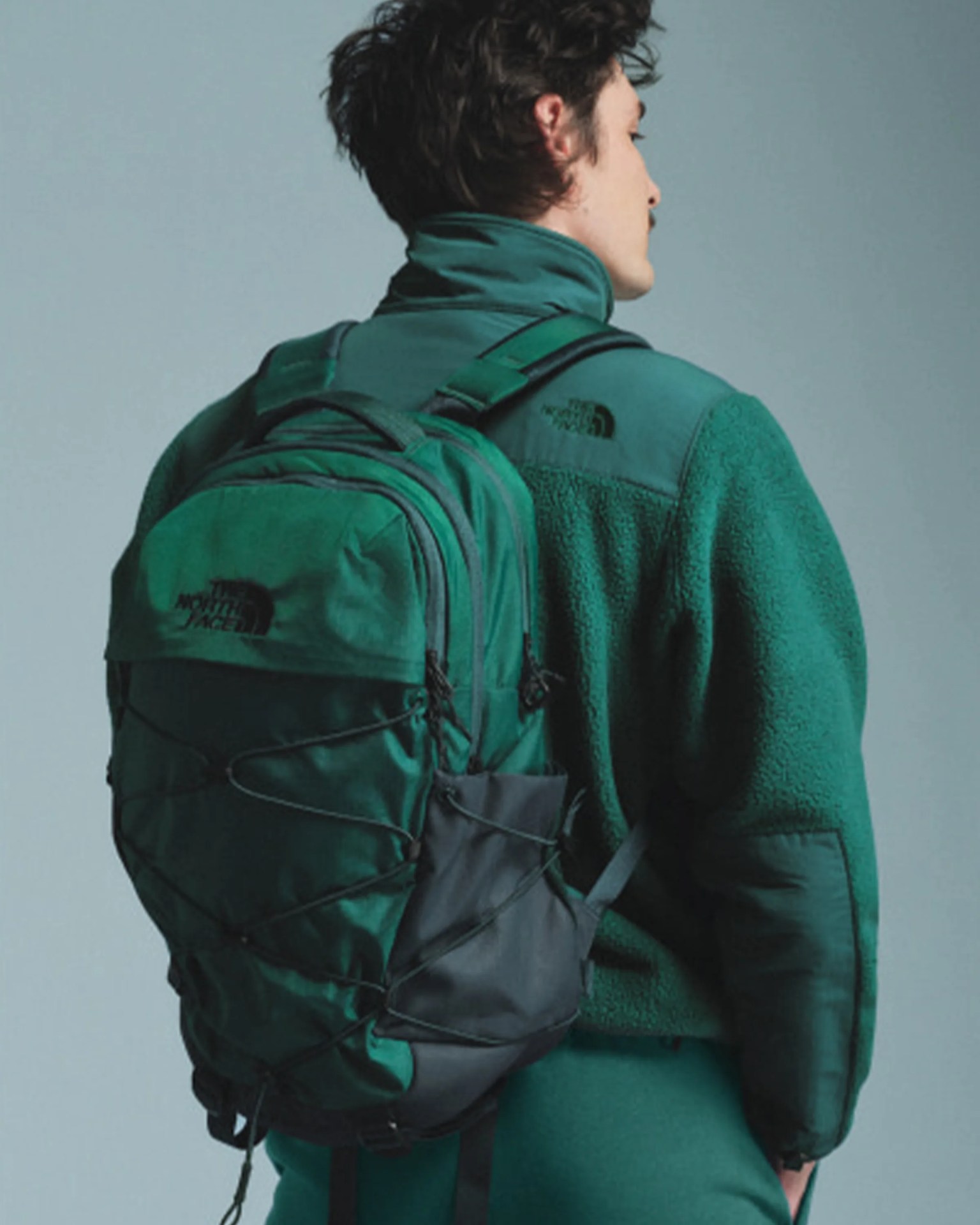 Green and black The North Face backpack worn by a person in a matching green fleece jacket.