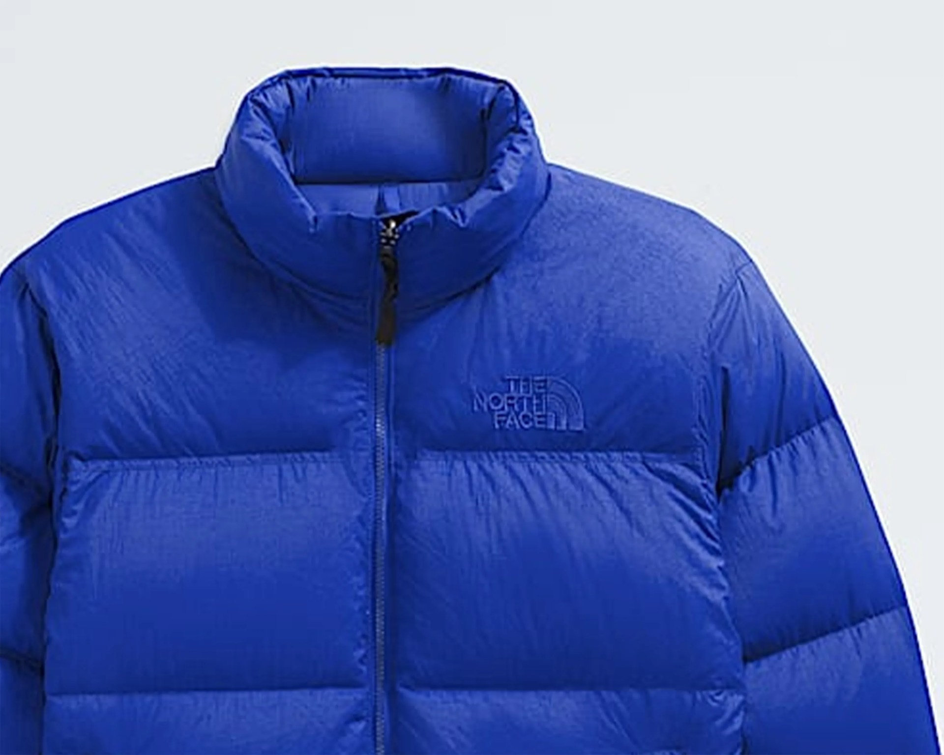 Blue puffer jacket with high collar and front zipper featuring The North Face logo on the chest.