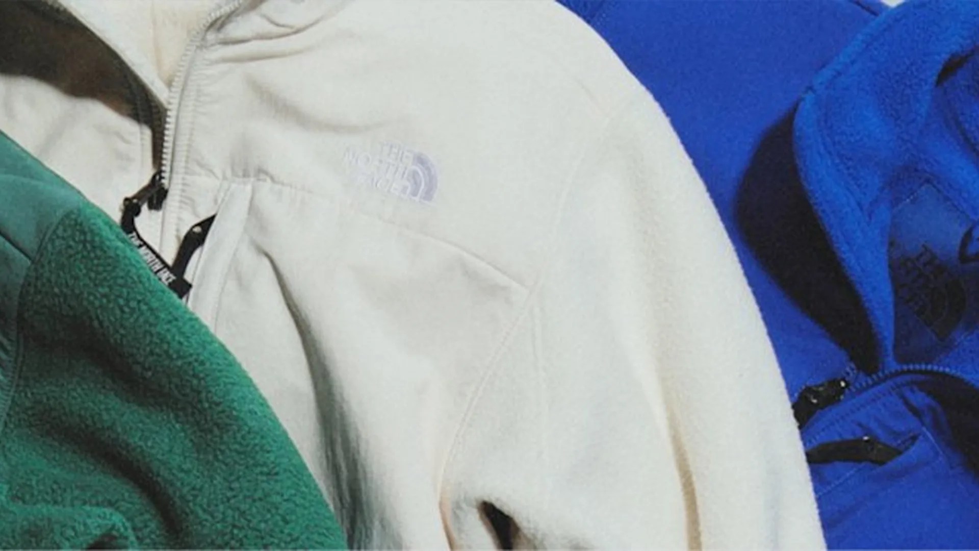 Three fleece jackets in green, off-white, and blue, each with The North Face logo and front zippers.