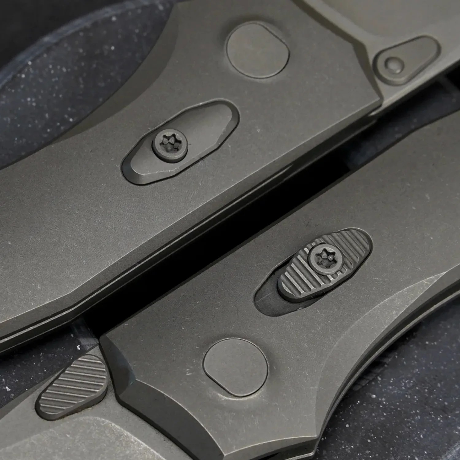 Close-up of two gray folding knife handles showing textured locking mechanisms and screws.