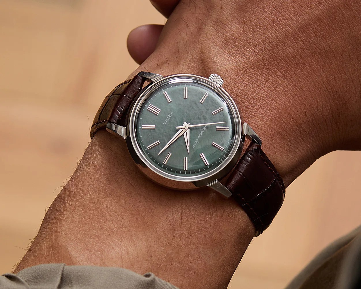Silver Timex wristwatch with a green dial and brown leather strap worn on a wrist.