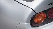 Close-up of a silver car's rear corner showing the tail light with orange and red sections and part of the "TO" letters from the brand name.