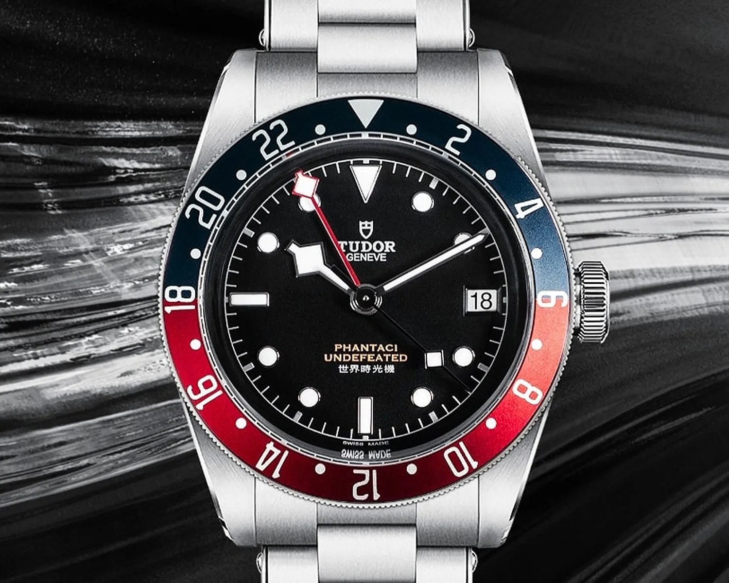 Stainless steel Tudor wristwatch with black dial, red and blue bezel, and date display at 3 o'clock.