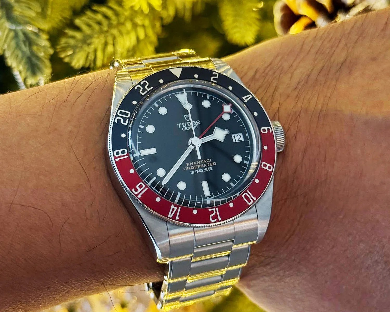 Stainless steel Tudor wristwatch with black and red bezel and black dial on a wrist.